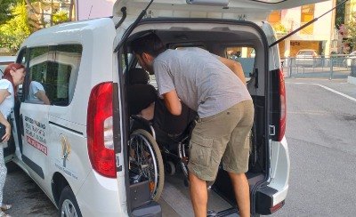 Un volontario carica una persona in carrozzina su un pulmino attrezzato